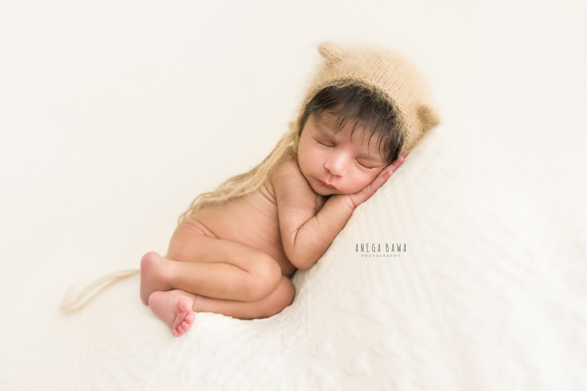 Newborn Photoshoot in Gurgaon: Brown Cap, White Backdrop, Sleeping Pose. Photographer: Anega Bawa, Delhi Noida.