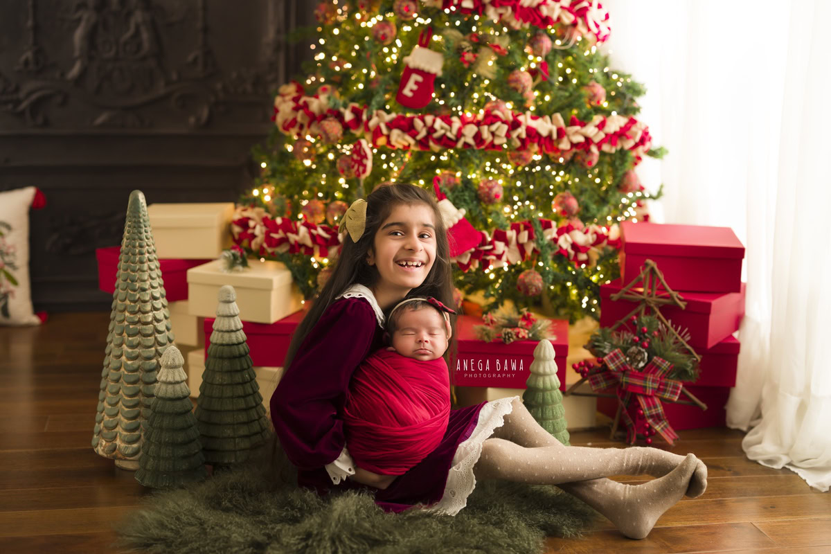 Newborn Photoshoot in Gurgaon: Red Wrap with Sibling and Xmas Tree. Photographer: Anega Bawa Photography, Delhi Noida.