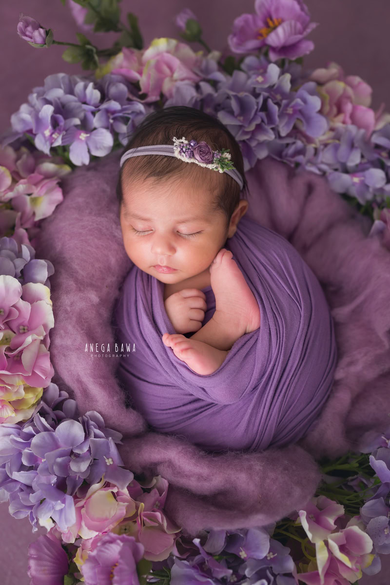 Newborn Photoshoot in Gurgaon: A baby wrapped in purple with lavender flowers, against a lavender backdrop. Photographer: Anega Bawa Photography, Delhi Noida.