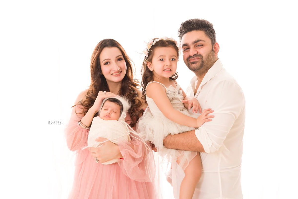 Newborn Photoshoot in Gurgaon: Family adorned in pink outfits, wrapped in white against a white backdrop. Photographer: Anega Bawa Photography, Delhi.