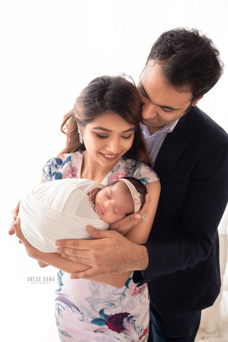 Newborn Photoshoot in Gurgaon: Family wrapped in white, captured against a white background. Photographer: Anega Bawa Photography, Delhi.