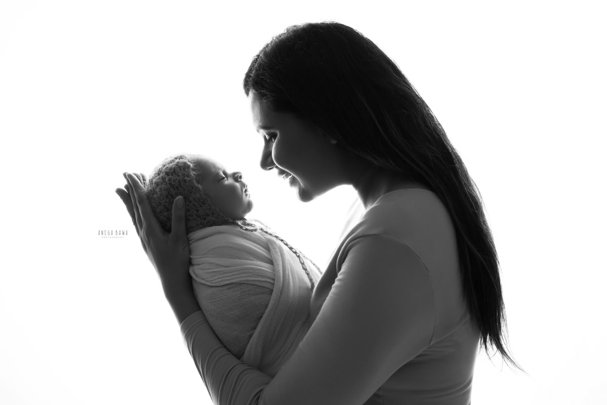 Newborn Photoshoot in Gurgaon: Mother holding the baby wrapped in white, captured in black and white. Photographer: Anega Bawa Photography, Delhi.