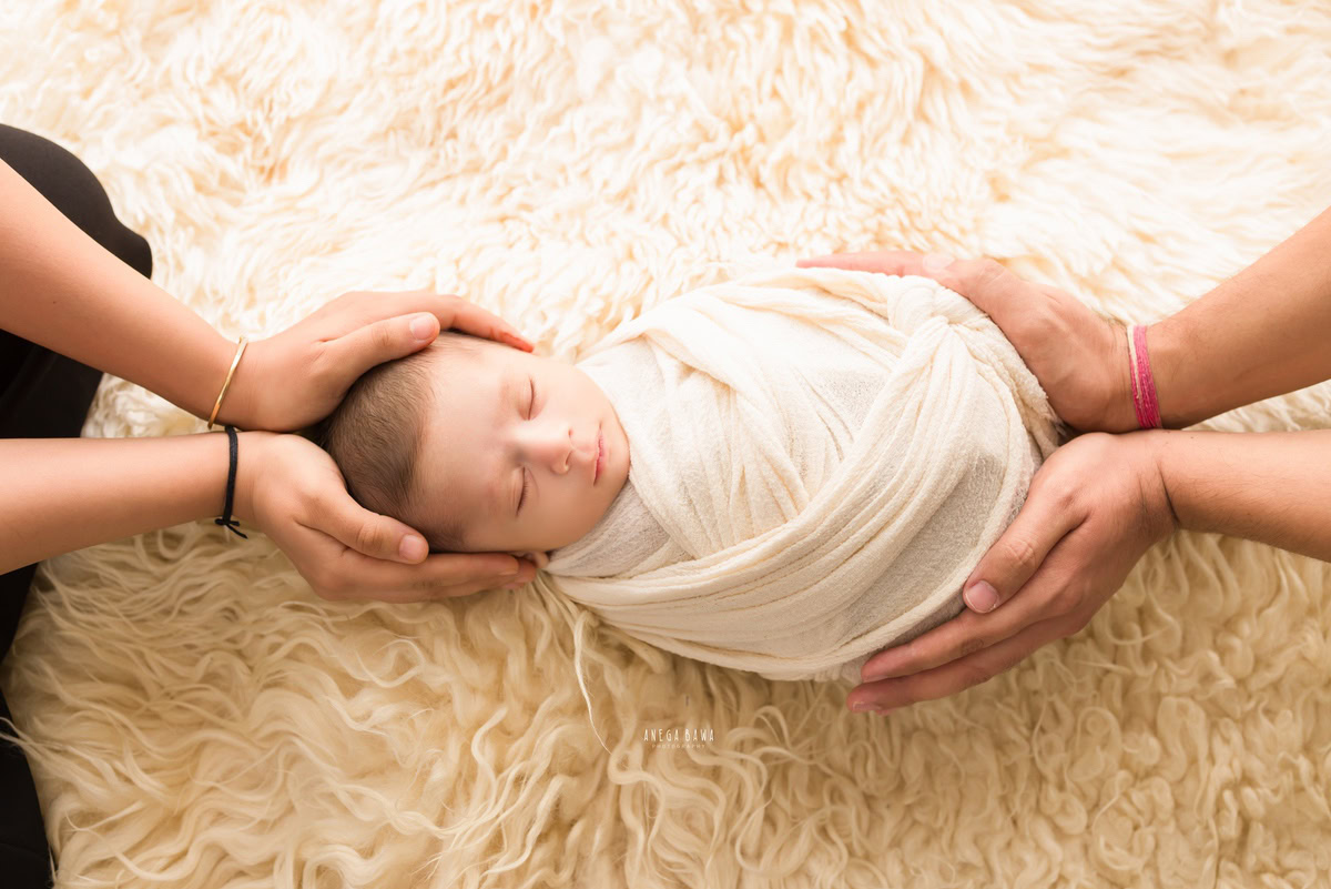 Newborn Photoshoot in Gurgaon: Mother and father's hands cradling the baby wrapped in white. Photographer: Anega Bawa Photography, Delhi.