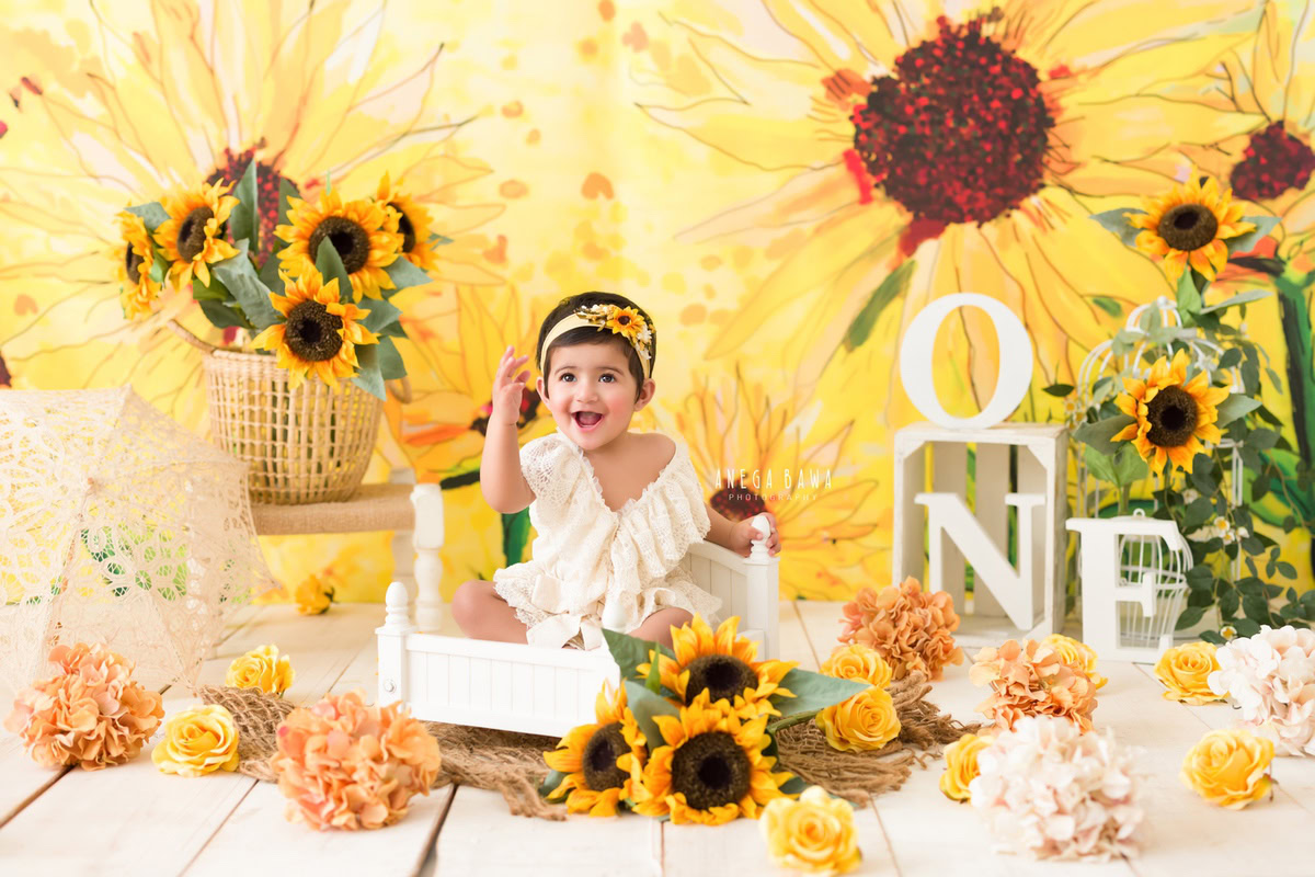 Indulge in the timeless charm of your little princess with a heartwarming sitter photography session in Delhi and Gurgaon by Anega Bawa Photography. Imagine your one-year-old darling seated against a delightful sunflower backdrop, accentuated by a sweet sunflower headband, all set on a cozy brown rug. Let Anega Bawa Photography capture these precious moments, preserving the innocence and joy of your little one for eternity. Trust us to craft enchanting memories that you'll treasure forever.