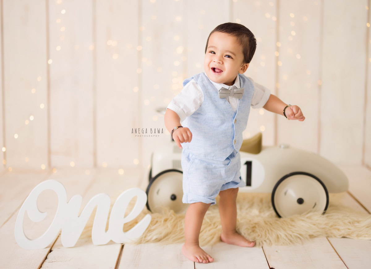 Capture the charm of your 1-year-old boy with Anega Bawa Photography in Delhi and Gurgaon. Set against a cozy beige backdrop, this sitter photoshoot features a toy scooter, fairy lights, and a beige rug, creating an enchanting scene that highlights the innocence and joy of your little one.