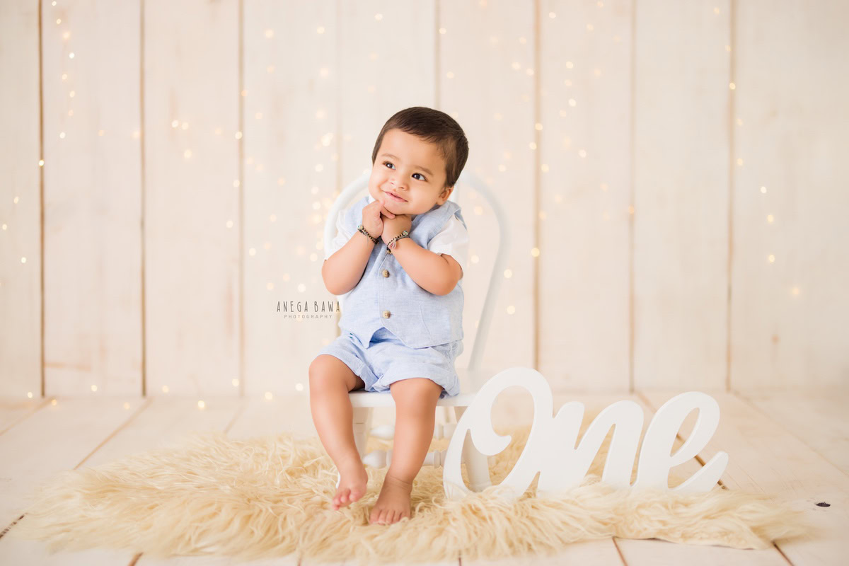 For a sitter photo shoot in Delhi and Gurgaon by Anega Bawa, a 1-year-old boy is elegantly captured sitting on a white chair, placed on a beige rug. The backdrop is a soft beige, creating a harmonious and timeless setting. This serene and stylish composition highlights the boy's innocence and charm, making it a perfect memory to cherish.