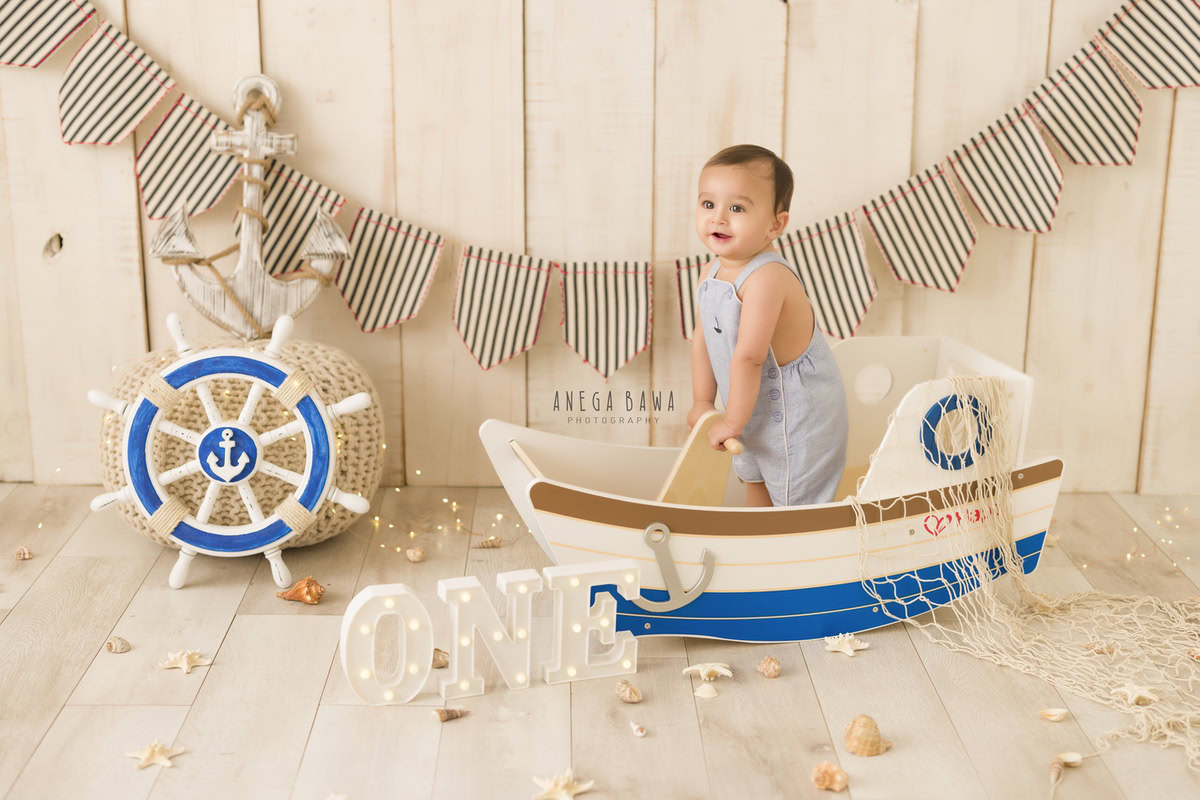 Adorable one-year-old boy in a charming toy spaceship, set against a soft beige backdrop with delicate petals on the floor, capturing his first birthday photoshoot in Delhi, by Anega Bawa, Gurgaon, Noida