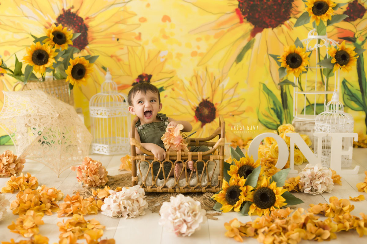 Anega Bawa captures a 1-year-old boy in a wooden basket, set against a sunflower backdrop and white castles. This delightful toddler photoshoot in Delhi, Gurgaon, and Noida showcases a perfect blend of natural beauty and whimsical charm.