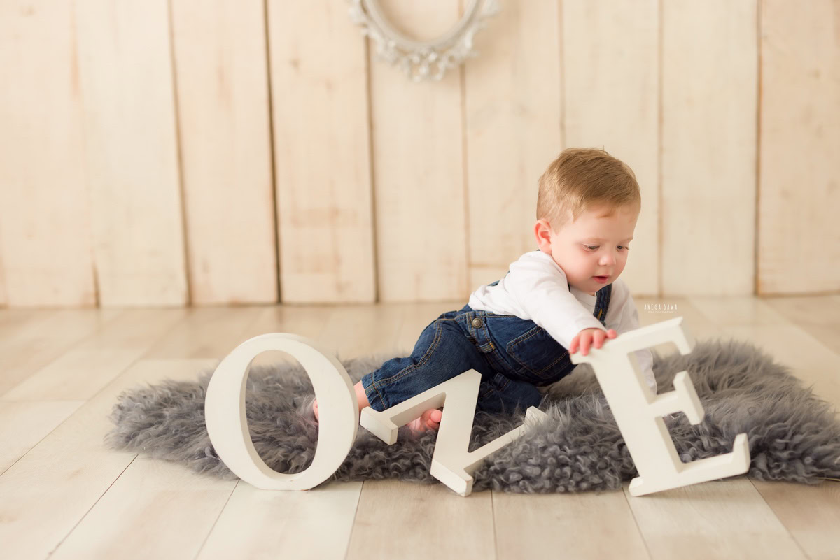 One-year-old boy lying on a grey rug against a beige backdrop, marking the serene ambiance of his pre-birthday photoshoot in Delhi by Anega Bawa, Gurgaon, Noida.