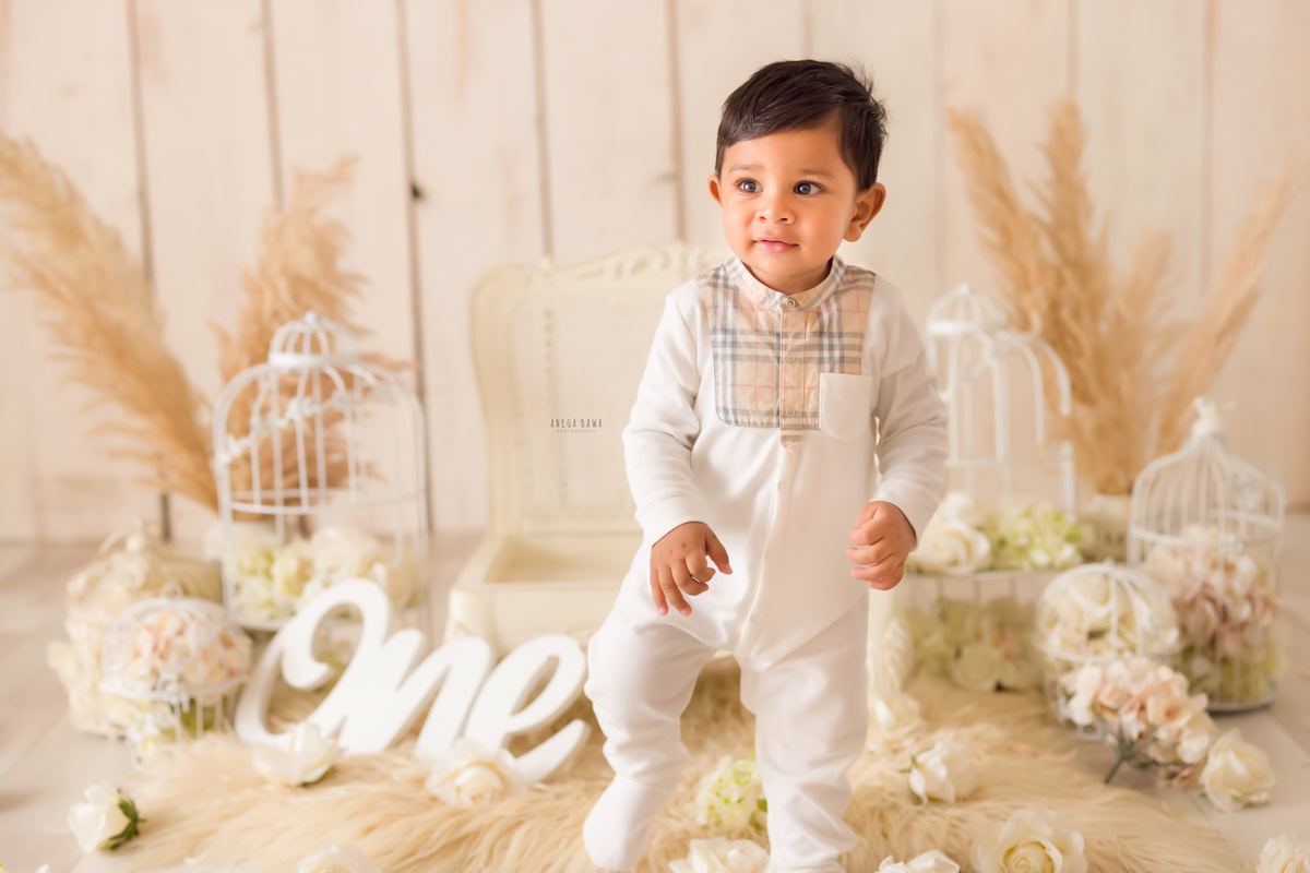 One-year-old boy on a beige rug surrounded by white castles and bushes against a beige backdrop, capturing the enchantment of his pre-birthday photoshoot in Delhi by Anega Bawa, Gurgaon, Noida.