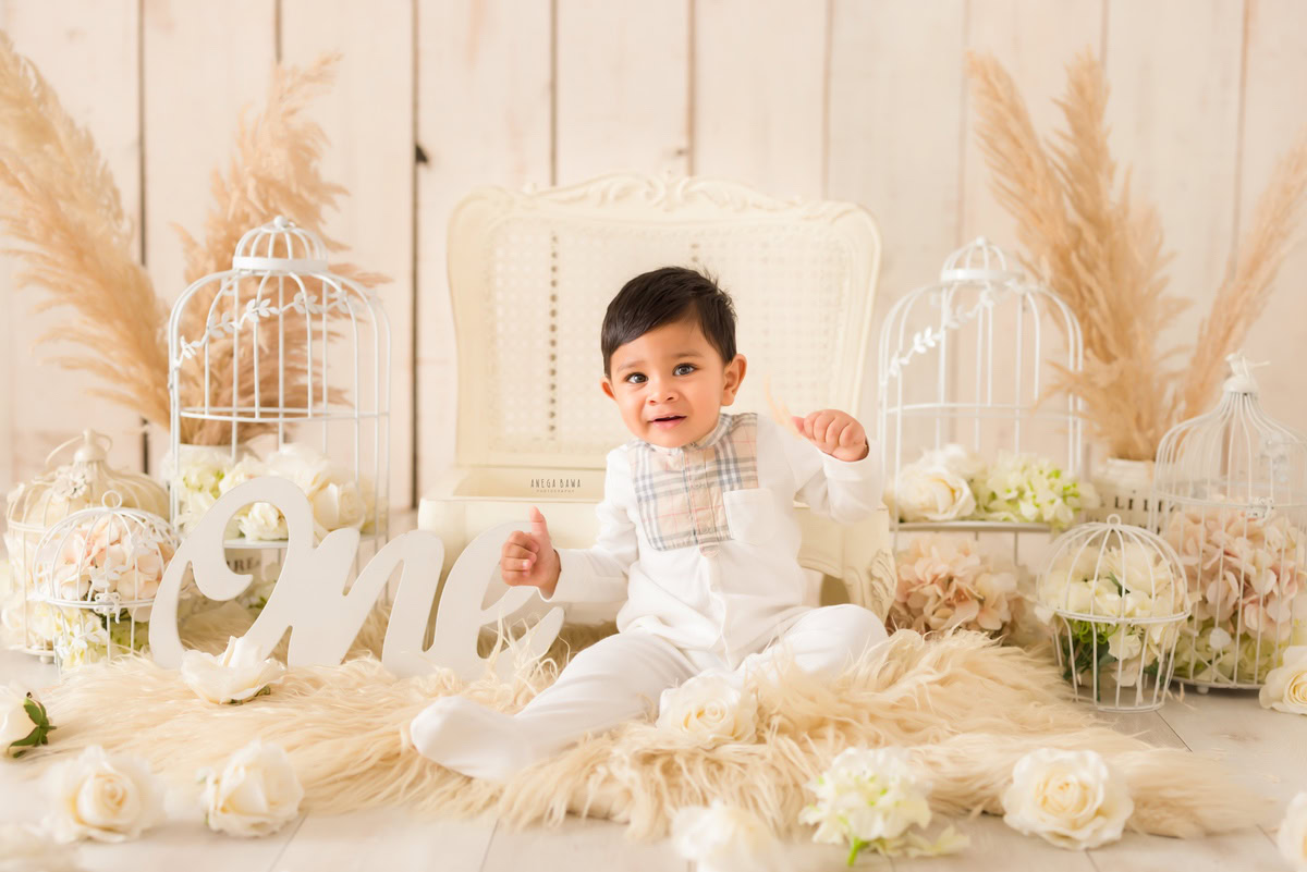 One-year-old boy on a beige rug surrounded by white castles and bushes against a beige backdrop, encapsulating the charm of his pre-birthday photoshoot in Delhi by Anega Bawa, Gurgaon, Noida.