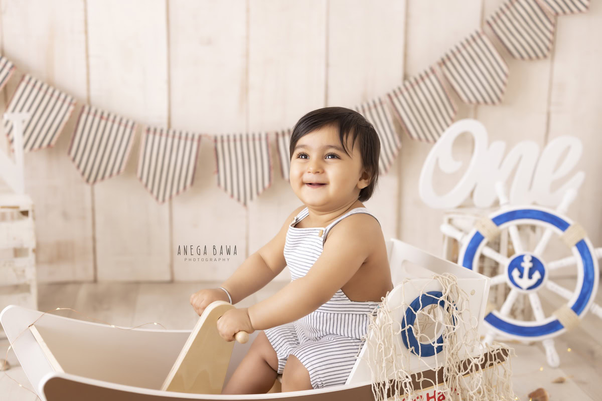 Embark on a cosmic adventure with your one-year-old as he sets sail on a toy space boat, captured against a serene beige backdrop by Anega Bawa Photography's sitter photography services in Delhi and Gurgaon.