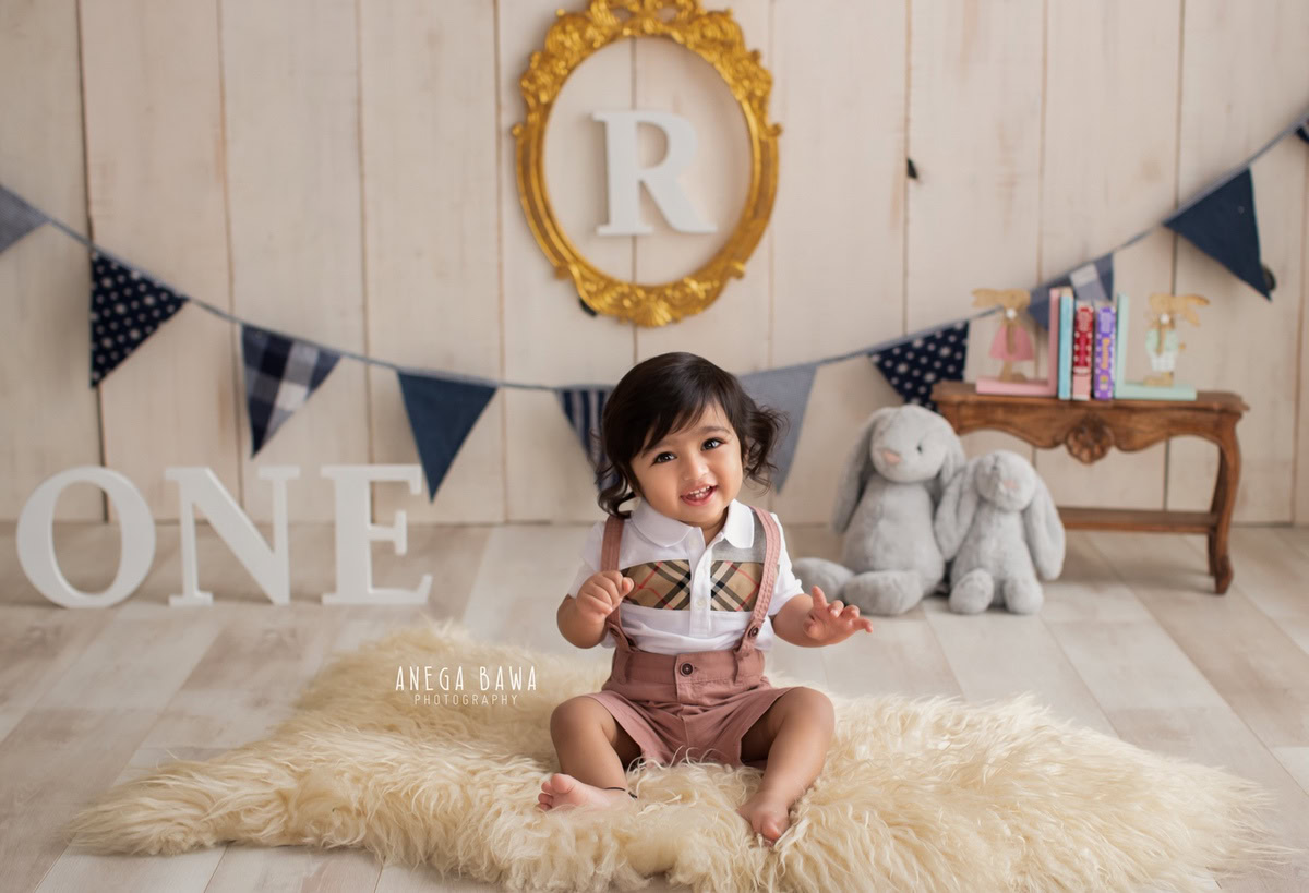 Capture the adorable moments of your 1-year-old boy with Anega Bawa Photography in Delhi and Gurgaon. Set against a warm beige backdrop, this sitter photoshoot features your little one seated on a beige rug, surrounded by teddy bears and an alphabet frame on the wall, creating a charming and memorable scene.