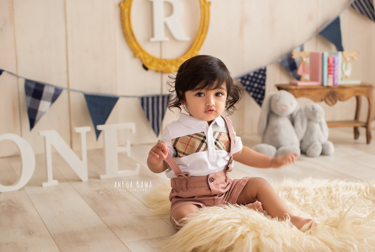 Capture precious moments with a sitter photoshoot of your 1-year-old boy by Anega Bawa Photography in Delhi and Gurgaon. Set against a cozy beige backdrop, your little one sits on a beige rug, surrounded by teddy bears and an alphabet frame on the wall, creating a charming and memorable scene.