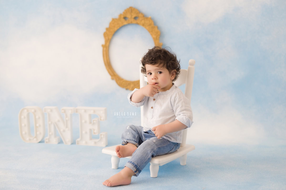 Watch your little prince perch on a white chair against a dreamy cloudy backdrop, with a golden frame adorning the wall behind him. Let Anega Bawa Photography in Delhi and Gurgaon capture this precious moment with their expert sitter photography services.