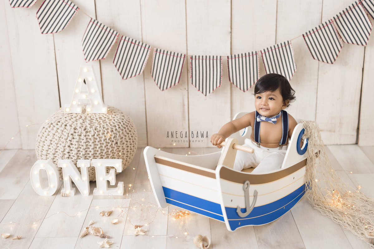 Captivating one-year-old boy seated in a charming toy spaceship, set against a soft beige backdrop, framed by an alpha-te frame, immortalizing his delightful first birthday photoshoot in Delhi, by Anega Bawa, Gurgaon, Noida