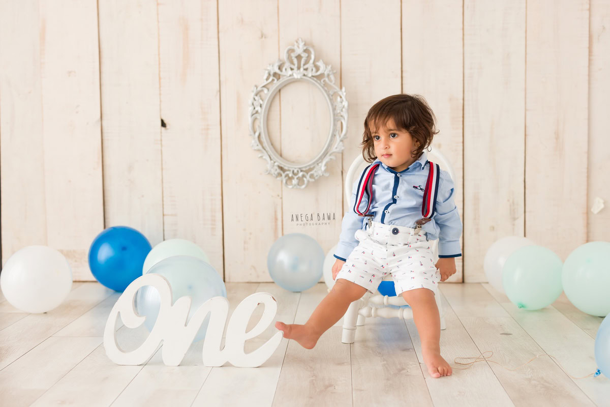 Behold your 1-year-old boy seated on a chair, framed by shimmering silver balloons against a soothing beige backdrop. Let Anega Bawa Photography in Delhi and Gurgaon preserve this delightful moment with their expert sitter photography services.