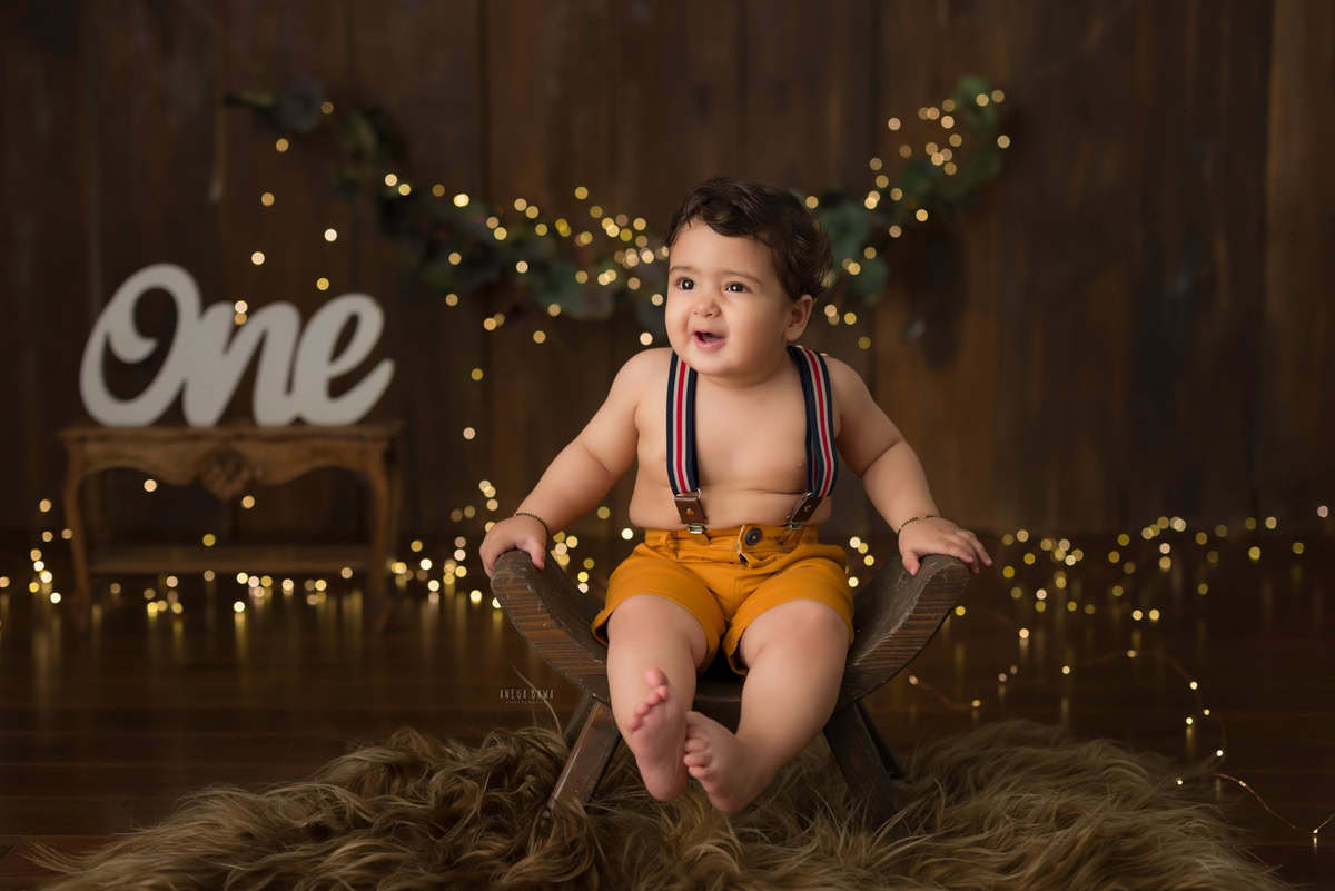 Capture the adorable essence of your 1-year-old boy as he sits on a curvy wooden chair, surrounded by twinkling fairy lights, set against a warm brown backdrop. Let Anega Bawa Photography in Delhi and Gurgaon create timeless memories with their expert sitter photography services.