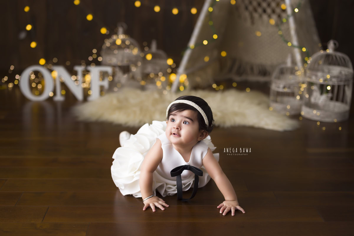 Adorable one-year-old girl joyfully crawling on a cozy beige rug, with white castles peeking from a net tent, set against a warm brown backdrop, commemorating her delightful first birthday photoshoot in Delhi, by Anega Bawa, Gurgaon, Noida