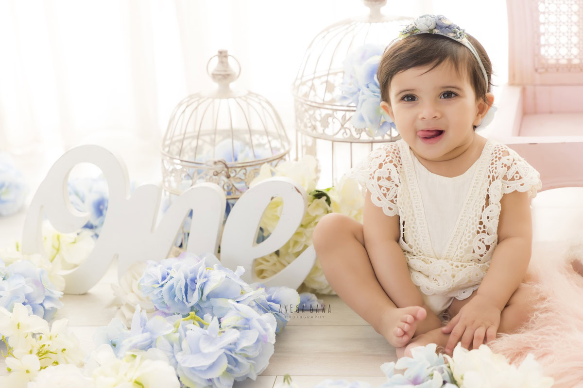 Immerse yourself in the magical world of your one-year-old princess with a heartwarming sitter photoshoot by Anega Bawa Photography in Delhi and Gurgaon. Watch as she sits gracefully amidst white castles and delicate blue and white flowers, her innocence radiating against a pristine white backdrop. Let Anega Bawa Photography capture these precious moments, creating everlasting memories for you to treasure.