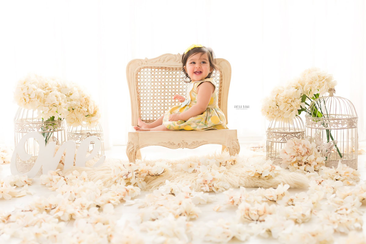 Experience the magic of your little one's milestones with a heartwarming sitter photography session in Delhi and Gurgaon by Anega Bawa Photography. Picture your one-year-old princess seated gracefully on a wooden ivory chair, surrounded by delicate ivory flowers and enchanting white castles against a pristine white backdrop. Let Anega Bawa Photography capture these precious moments, creating timeless memories for you to cherish forever. Trust us for an unforgettable sitter photography experience in Delhi and Gurgaon, preserving the innocence and joy of your little princess.