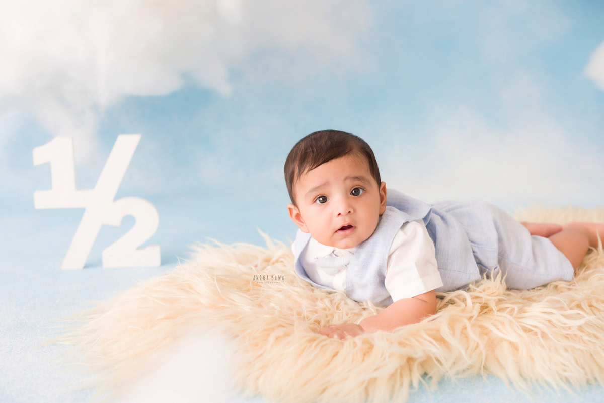 Captured by Anega Bawa, this heartwarming scene from a baby pre-birthday photoshoot in Delhi-Gurgaon-Noida features a 6-month-old boy lying on a cozy beige rug against a serene cloudy backdrop. The soft lighting and gentle ambiance beautifully complement the innocence and charm of the young child, creating a timeless and precious moment to cherish forever.