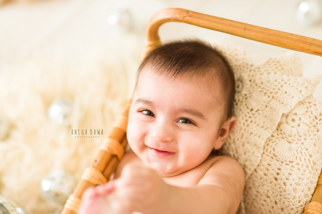 Capture the joy of your baby boy at 3, 4, 5, or 6 months against a beige backdrop with disco balls, showcasing his adorable smiling pose. Contact Anega Bawa for your baby boy's photo shoot in Delhi, Gurgaon, or Noida.