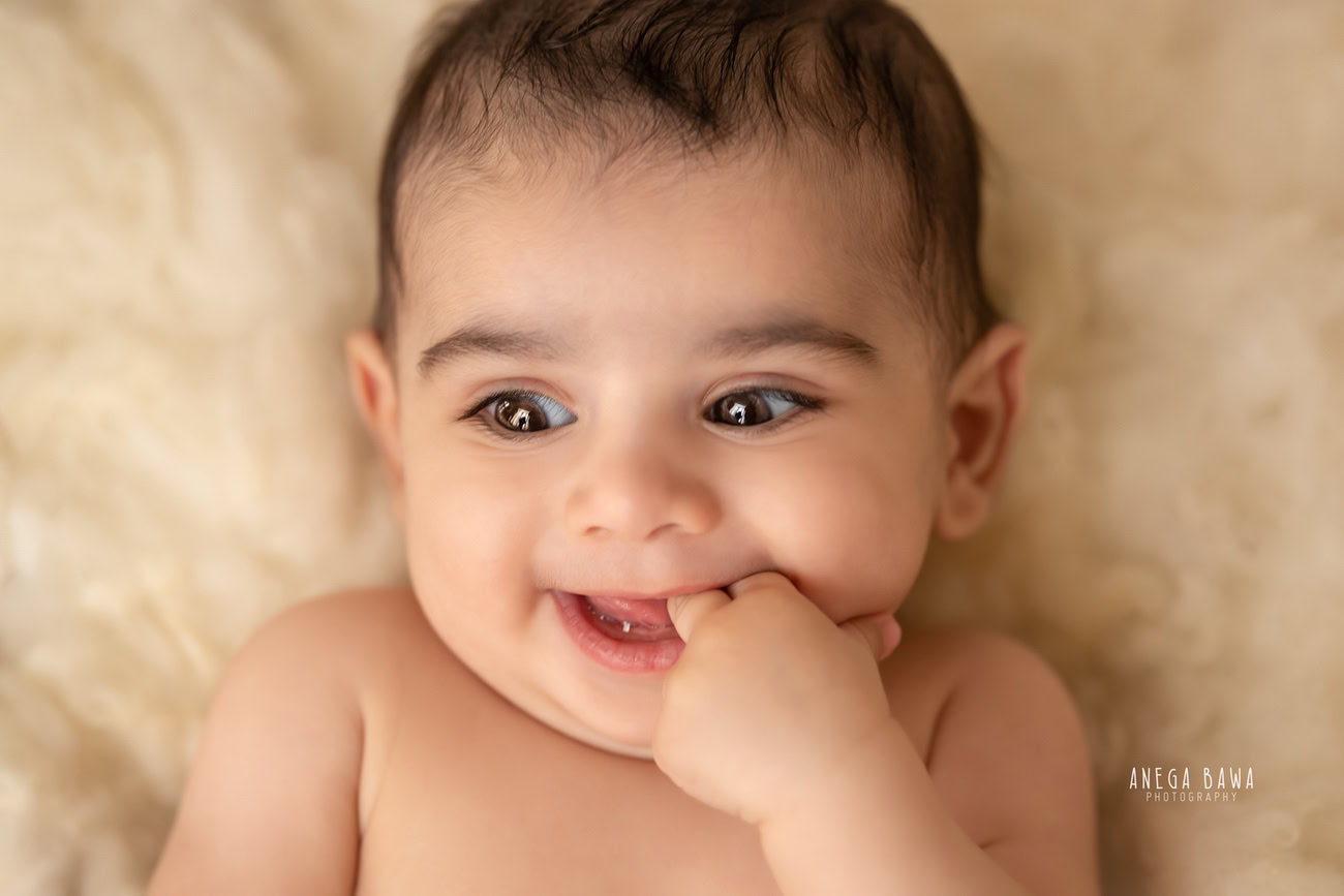 Cherubic 6, 5, 3, 4-month-old baby boy graces the lens with his adorable smile and captivating poses on a soft beige rug. Expertly captured by Anega Bawa, your trusted baby photographer in Delhi, Gurgaon, and Noida.