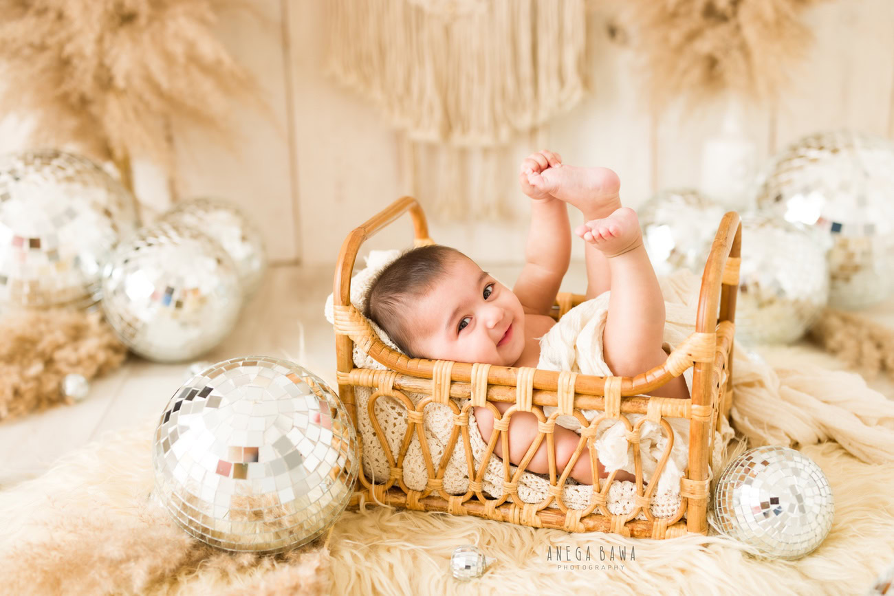 Create timeless memories of your 3, 4, 5, or 6-month-old baby boy wrapped in beige, lying on a cozy beige rug, surrounded by twinkling disco balls against a neutral backdrop. Book your session with Anega Bawa in Delhi, Gurgaon, or Noida.