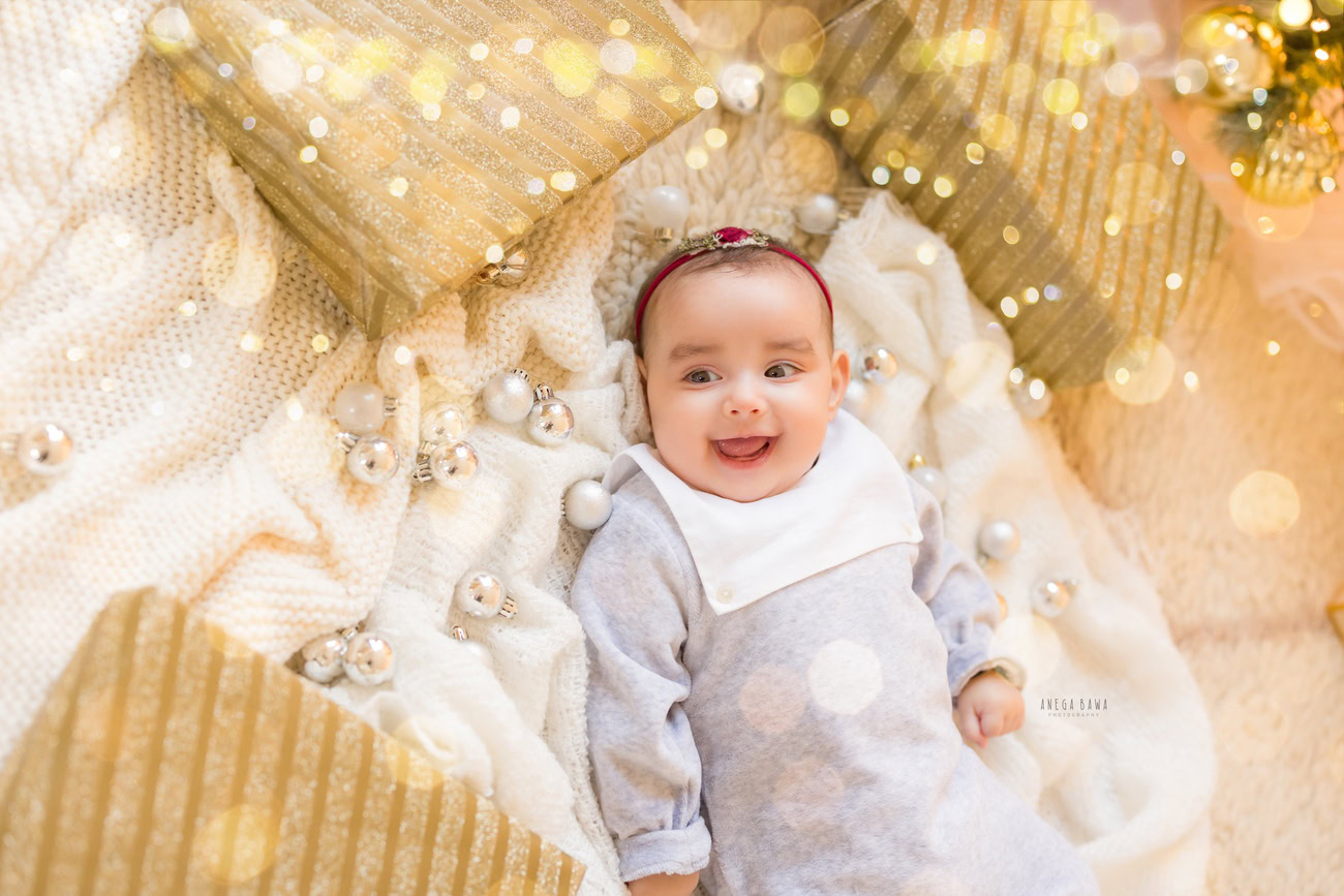 Adorable baby boy during a photoshoot wearing a blue and white baby boy suit, surrounded by golden lights and disco balls on a white backdrop. Location: Delhi, Gurgaon, Noida. Photographer: Anega Bawa.