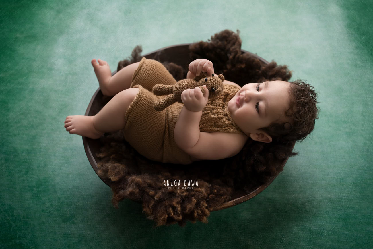 Captivating baby boy photo shoot capturing adorable 6, 5, 3, 4-month-old milestones with a charming brown basket, soft toy, and brown baby boy suit against a lush green backdrop. Masterfully orchestrated by Anega Bawa, your esteemed baby photographer in Delhi, Gurgaon, and Noida.