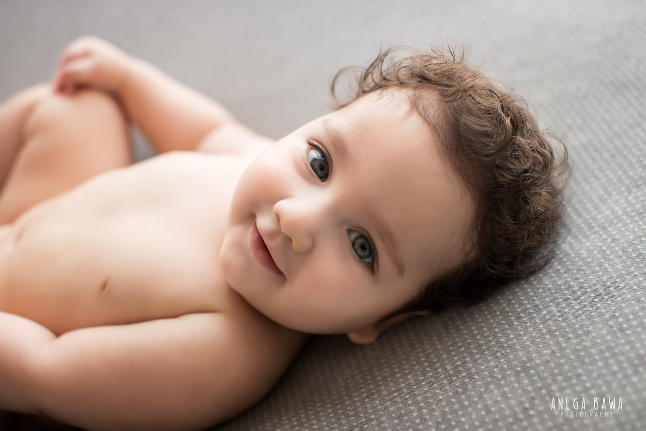 Enchanting baby boy photo shoot, featuring an endearing 6, 5, 4, 3-month-old in a sweet lying pose against a sophisticated grey backdrop. Expertly captured by Anega Bawa, the renowned baby photographer in Delhi, Gurgaon, and Noida.