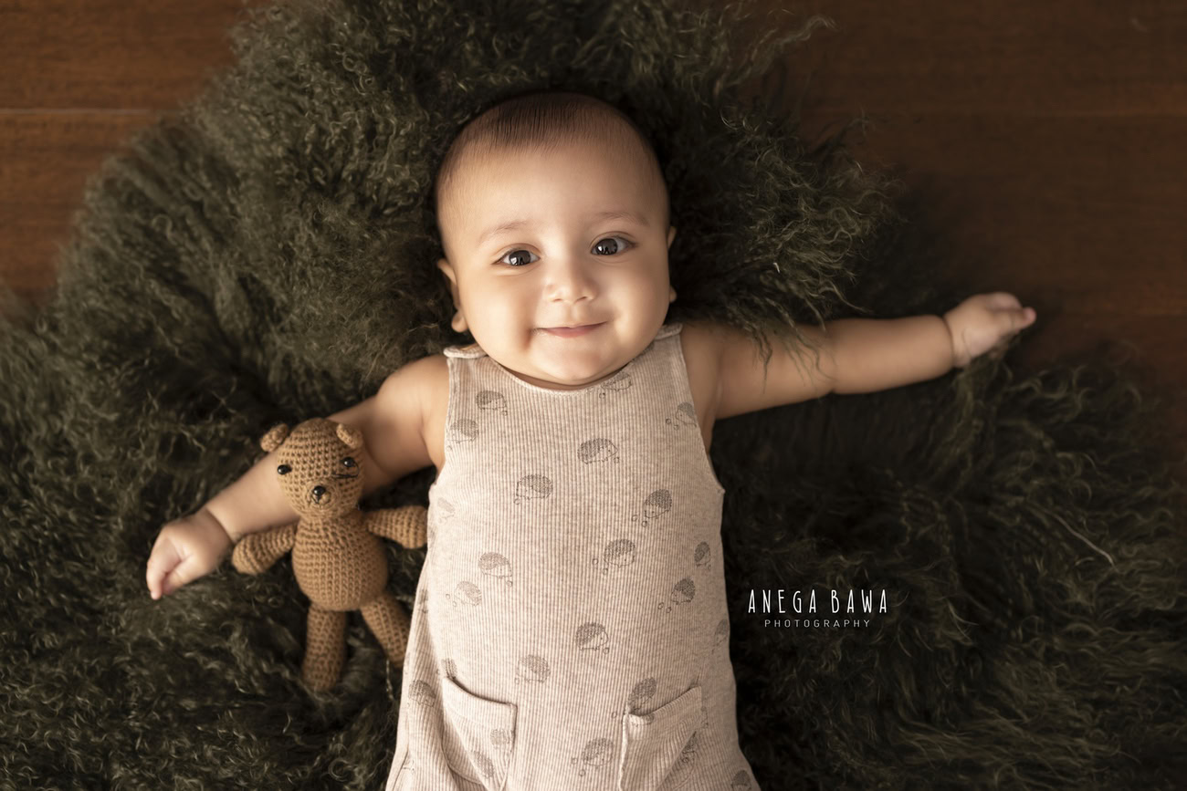 Experience the charm of your baby boy's innocence as he poses with his favorite soft toy on a lush green rug against a soothing brown backdrop. Contact Anega Bawa for a heartwarming baby boy photoshoot in Delhi, Gurgaon, or Noida.