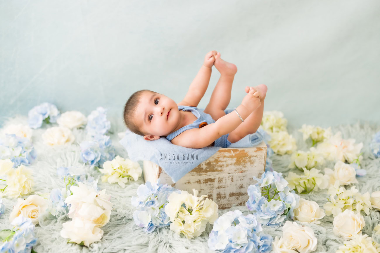 Capture the adorable moments of your little boy's innocence with a grey rug, adorned with blue and white flowers, set against a serene grey backdrop. Contact Anega Bawa for a delightful baby boy photoshoot in Delhi, Gurgaon, or Noida.