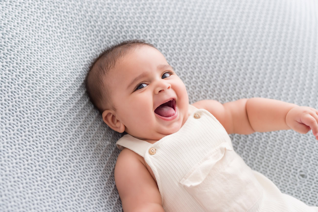 Baby boy photo shoot, 6, 5, 3, or 4 months, white baby boysuit, grey backdrop, cute laughing pose. Location: Delhi, Gurgaon, Noida. Photographer: Anega Bawa.