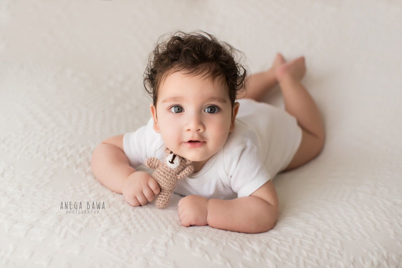 Elegant baby boy photo shoot capturing the innocence of 6, 5, 3, 4-month-old milestones in a pristine white baby boy suit, accompanied by a soft toy against a pure white backdrop. Crafted with expertise by Anega Bawa, your trusted baby photographer in Delhi, Gurgaon, and Noida.