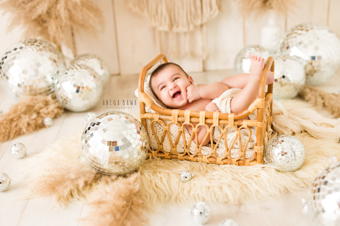 Immerse your little prince in a world of wonder with a captivating photoshoot! Picture him nestled in a charming wooden cot atop a soft beige rug, surrounded by twinkling discoballs against a soothing beige backdrop. Contact Anega Bawa to capture these precious moments in Delhi, Gurgaon, or Noida.