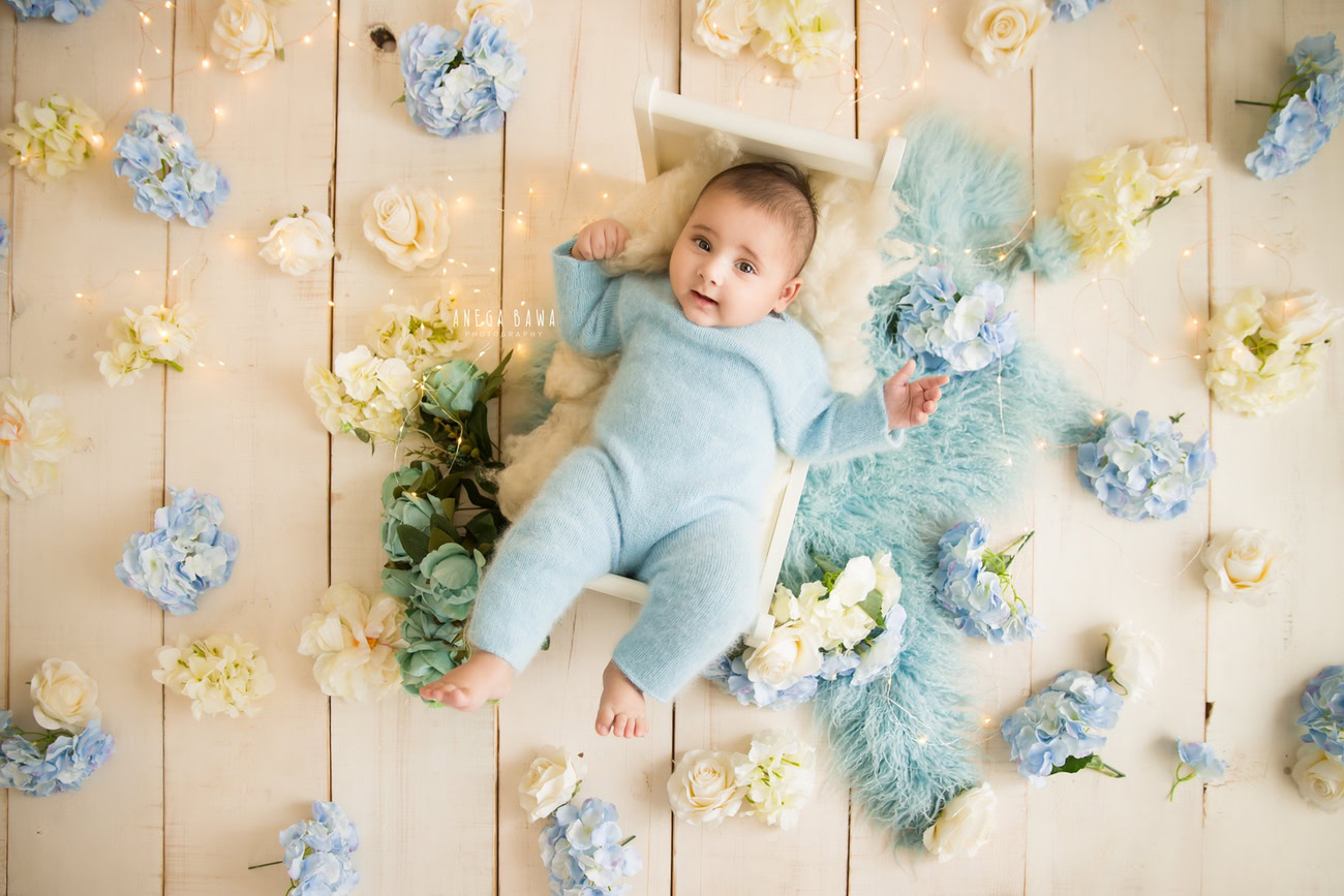 Capture the innocence of your little prince in a charming blue baby boysuit amidst blue and white flowers against a soft beige backdrop. Trust Anega Bawa for exquisite baby photography in Delhi, Gurgaon, or Noida.