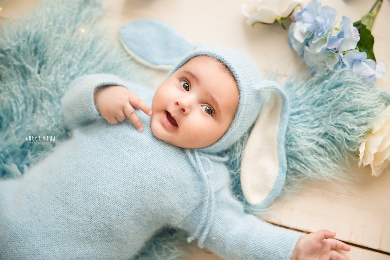 Capture the precious moments of your little prince, aged 6, 4, 3, or 5 months, in a delightful blue cap, nestled on a soft blue rug, against a soothing beige backdrop. Contact Anega Bawa for timeless baby photography in Delhi, Gurgaon, or Noida.