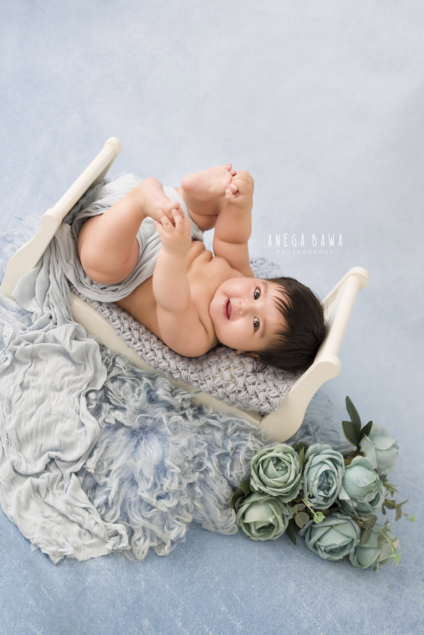 Baby boy photographer, 6, 4, 3, or 5 months, grey wrap, blue backdrop, green flowers. Location: Delhi, Gurgaon, Noida. Photographer: Anega Bawa.