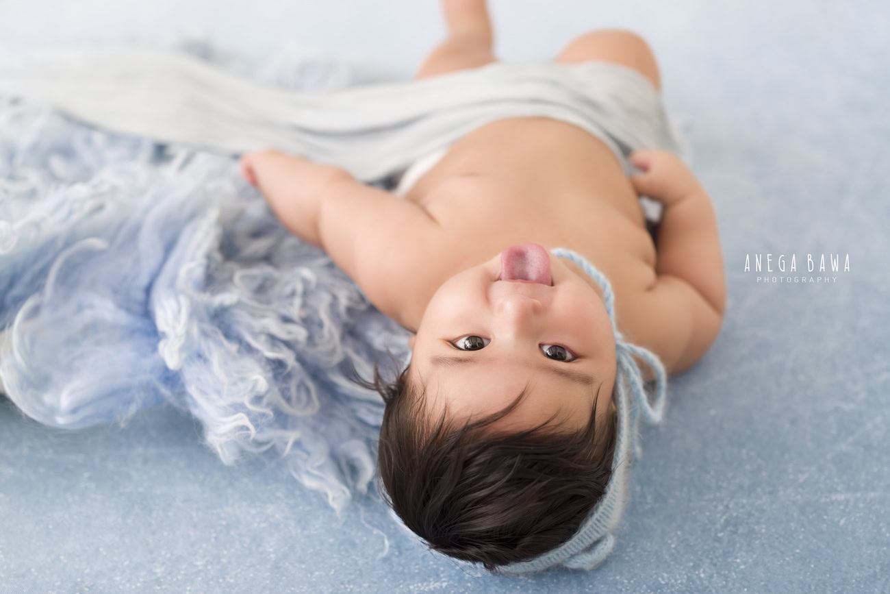 Capture the charm of your 6, 4, 3, or 5-month-old baby boy in a cute pose, wrapped in grey fabric, against a blue rug and grey backdrop. Contact Anega Bawa for an unforgettable photoshoot in Delhi, Gurgaon, or Noida.