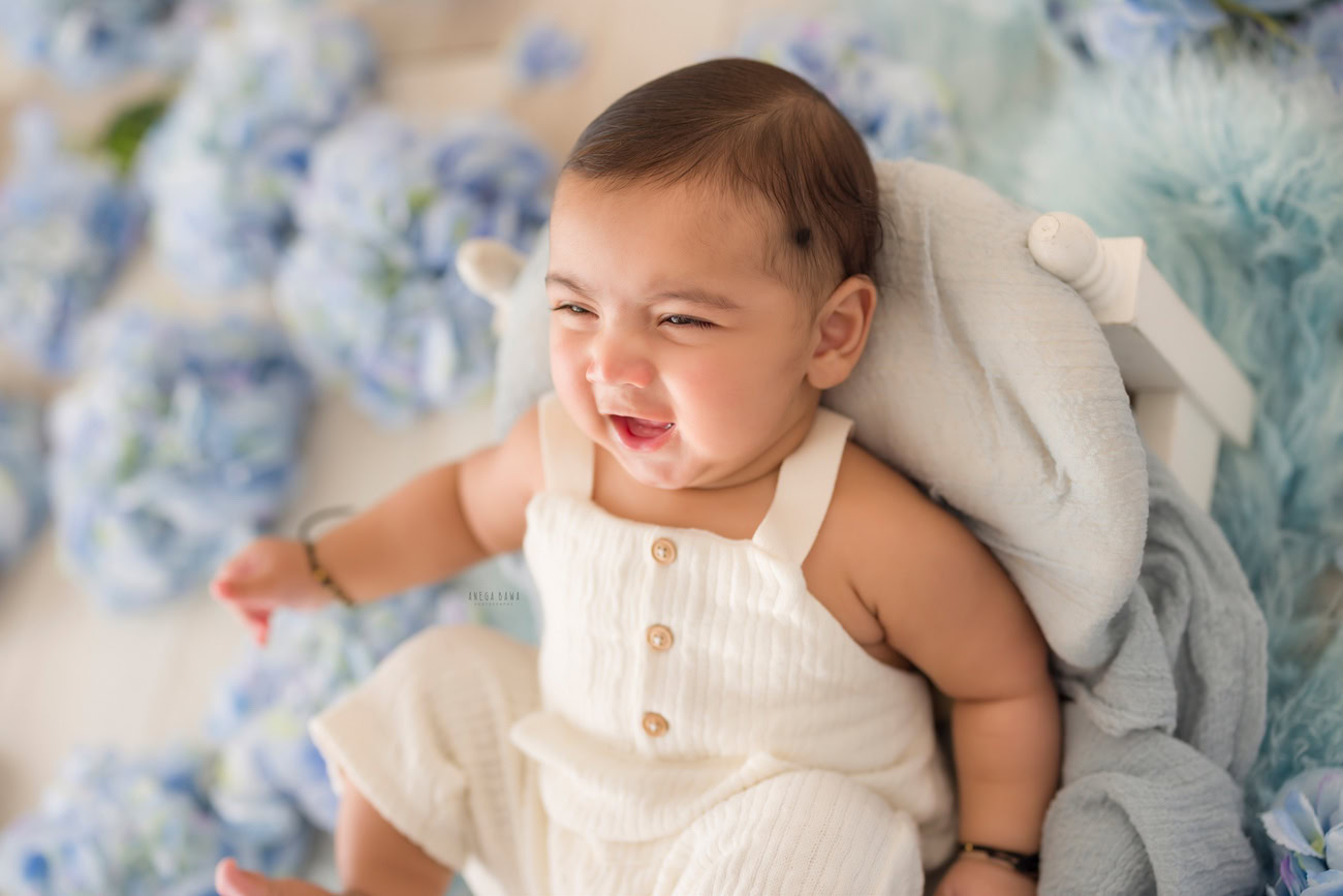 Baby boy photographer, 6 or 4 or 3 or 5 months, white baby boy suit, blue flowers, white backdrop. Location: Delhi, Gurgaon, Noida. Photographer: Anega Bawa.
