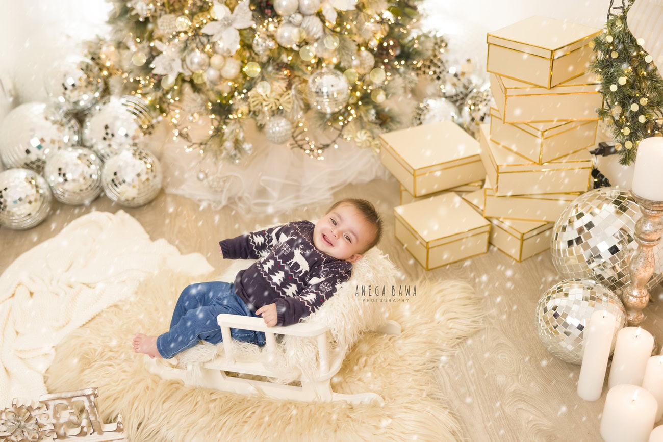 Create everlasting memories of your 6, 4, 3, or 5-month-old baby boy in an adorable Christmas-themed photoshoot, featuring a festive jumper, Xmas tree, gifts, and disco balls, set against a beige rug and backdrop. Book your session with Anega Bawa in Delhi, Gurgaon, or Noida.