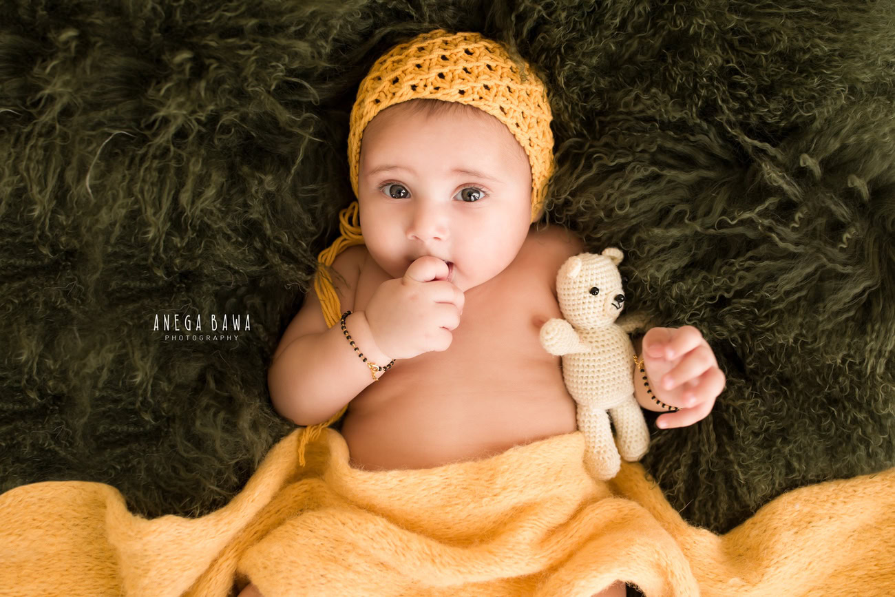 Capture the precious moments of your 6, 4, 3, or 5-month-old baby boy wrapped in a vibrant yellow wrap, adorned with a cute yellow cap, against a serene green backdrop, with a white soft toy. Contact Anega Bawa for your baby boy's photography session in Delhi, Gurgaon, or Noida.