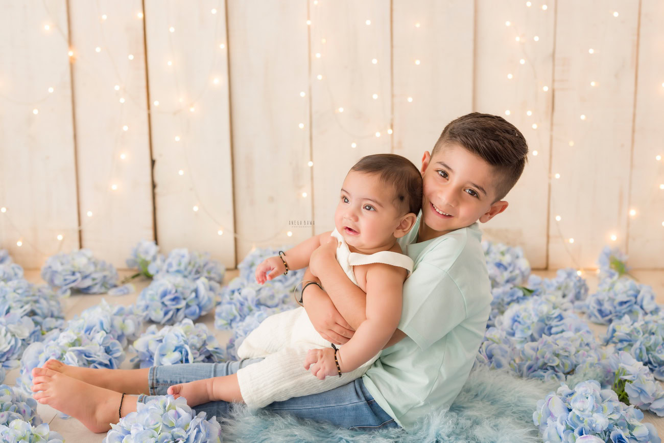 Baby boy photography, 5 or 4 or 3 or 6 months, beige backdrop, blue flowers, sibling, golden lights. Location: Delhi, Gurgaon, Noida. Photographer: Anega Bawa.