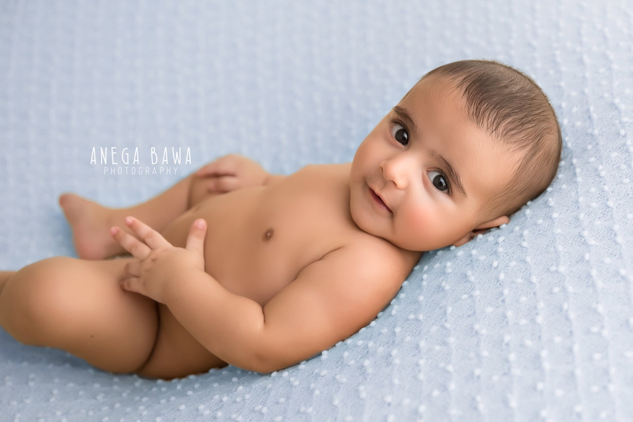 Captivating baby boy photography session showcasing the playful innocence of a 5, 4, 3, 6-month-old against a serene blue backdrop, capturing those mischievous glances. Crafted with expertise by Anega Bawa, your trusted baby photographer in Delhi, Gurgaon, and Noida.