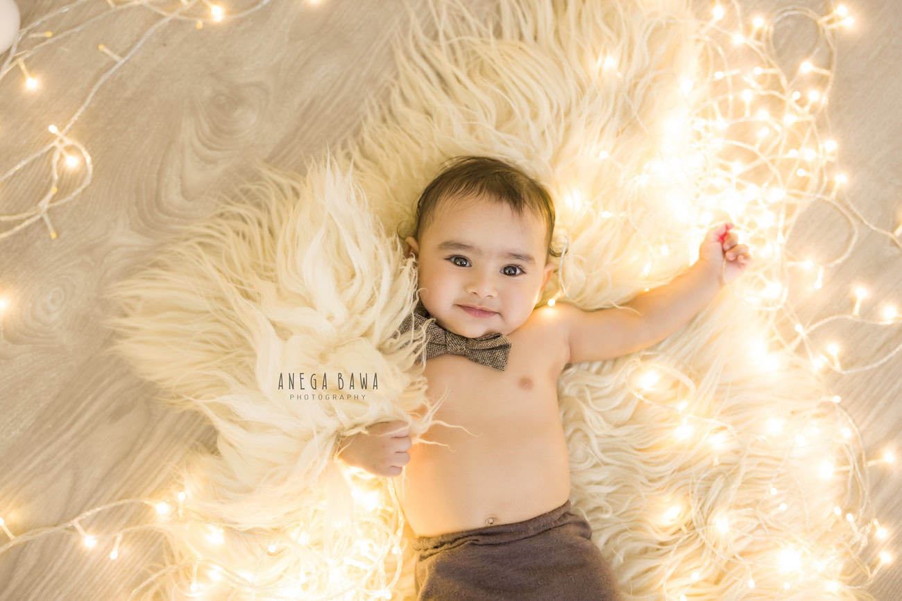 Highlight the charm of your little boy aged 3, 4, 5, or 6 months with Anega Bawa's delightful baby boy photography services in Delhi, Gurgaon, or Noida. Adorned with a cute bow, set against a cozy beige rug and bathed in the soft glow of golden lights, capture timeless moments against a serene beige backdrop.