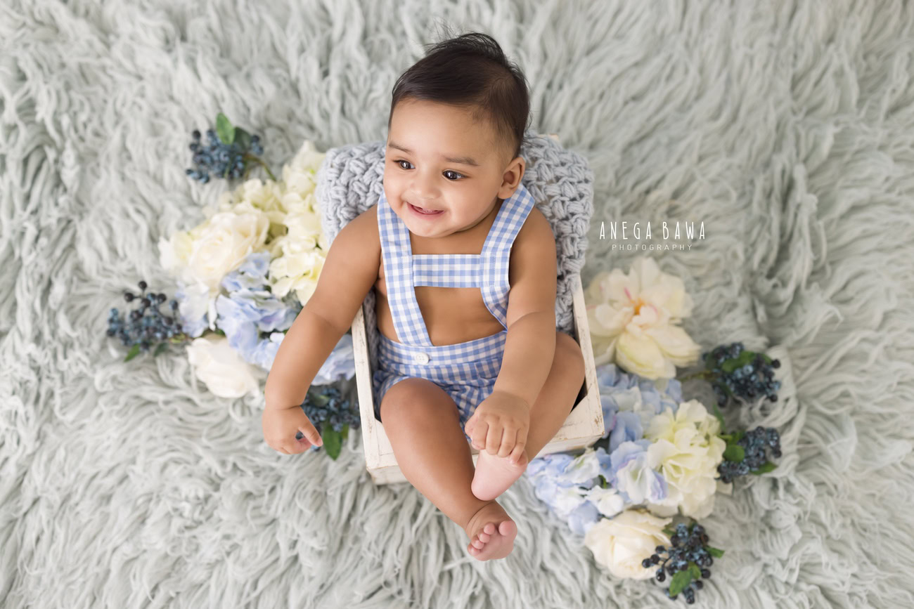 Capture the adorable moments of your baby boy, aged 3, 4, 5, or 6 months, with Anega Bawa's baby boy photography in Delhi, Gurgaon, or Noida. Featuring a charming grey rug adorned with blue and white flowers, enjoy delightful seating poses against this serene backdrop.