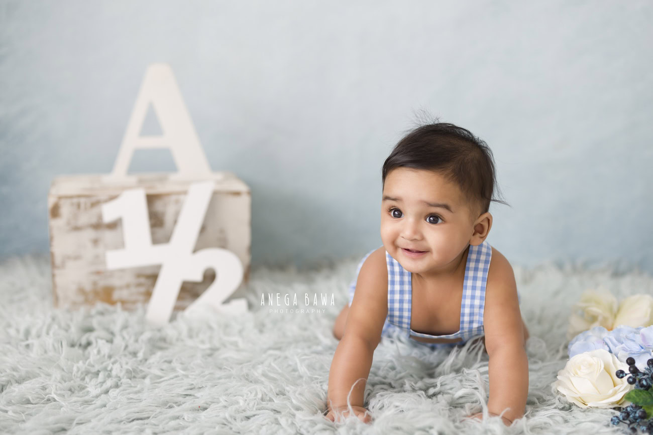 Delight in the innocence of your little one with Anega Bawa's baby boy photography in Delhi, Gurgaon, or Noida. This charming photoshoot captures your baby boy, aged 3, 4, 5, or 6 months, in a cute blue sleeveless baby boy suit, showcasing adorable crawling poses against a serene grey rug and backdrop.