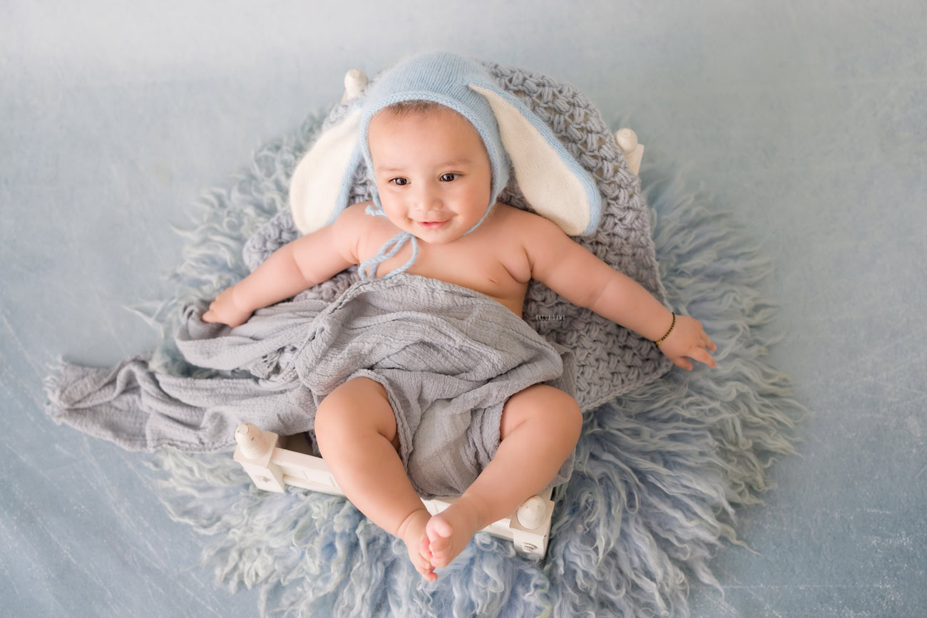 Baby boy photography, 5, 4, 3, or 6 months, cute cap, grey backdrop, seating pose. Location: Delhi, Gurgaon, Noida. Photographer: Anega Bawa.